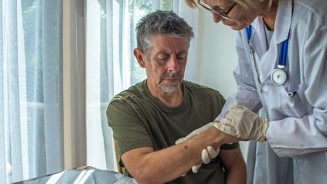 Ärztin hält den Arm eines Patienten und betrachtet diesen. 