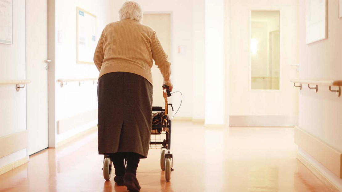 Ältere Frau schiebt einen Rollator durch die Gänge eines Pflegeheims.