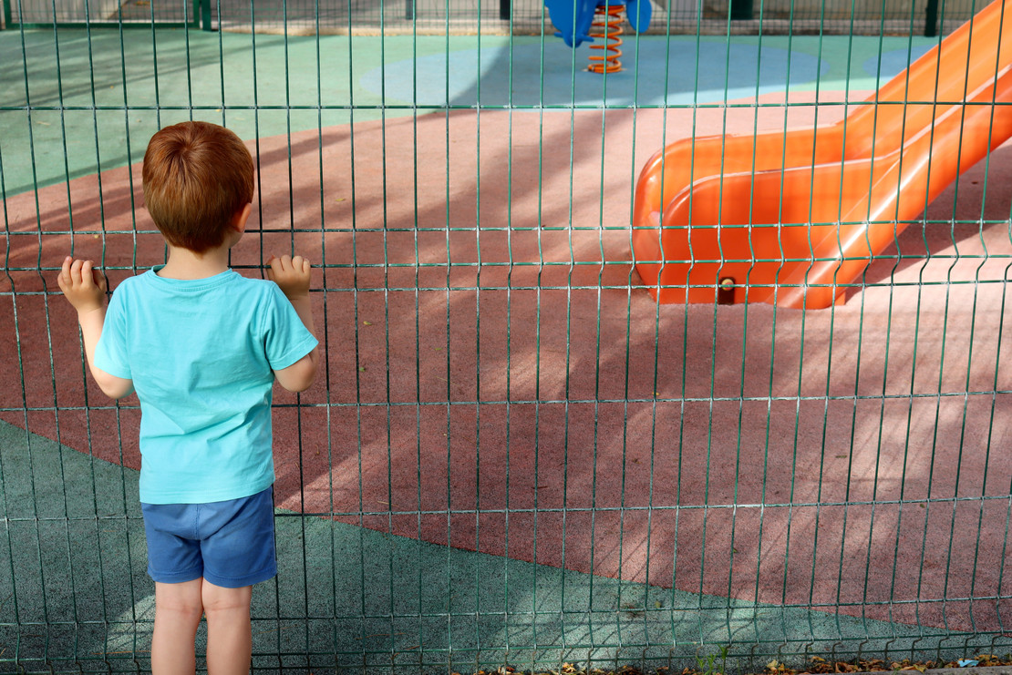 Kind steht vor einem Zaun